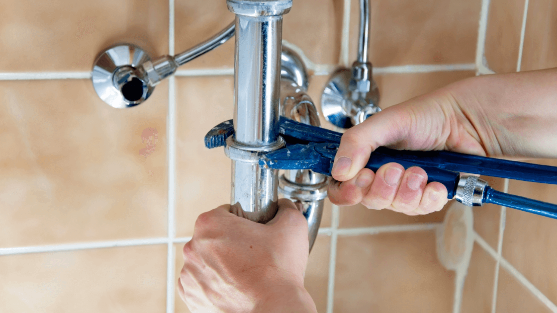 Hands using a wrench to tighten plumbing pipes, representing the impact of a plumbing career